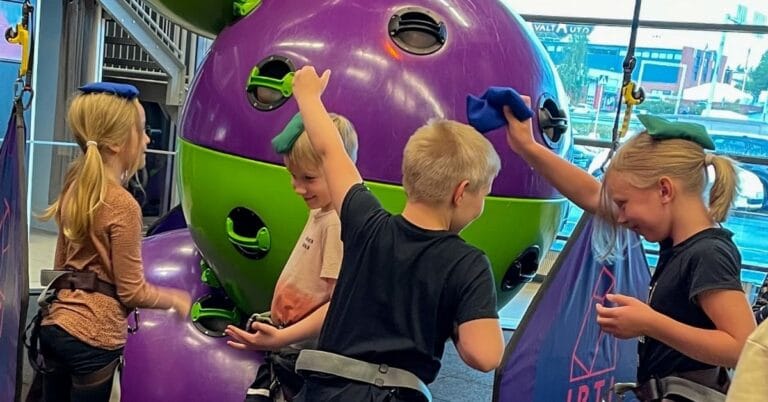 Koululaisryhmä seikkailupuistossa kiipeilemässä ja nauramassa yhdessä