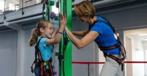 Luokkaretket ja kouluryhmät -artikkelikuvitus 1200 x 268 px 3 - Active Entertainment Lapsi ja aikuinen antavat läpyt toisilleen onnistuneen kiipeilyn jälkeen