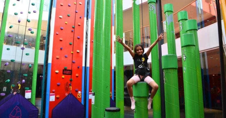 Nuori tyttö reippaana Irti Maasta-kiipeilykeskuksen tolpilla